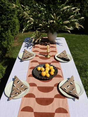 Garden tablescape with a pink and brown table runner and taupe linen napkins.
