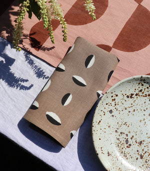 Close-up of a hand block printed linen napkin in a taupe color with a black and white geometric pattern.